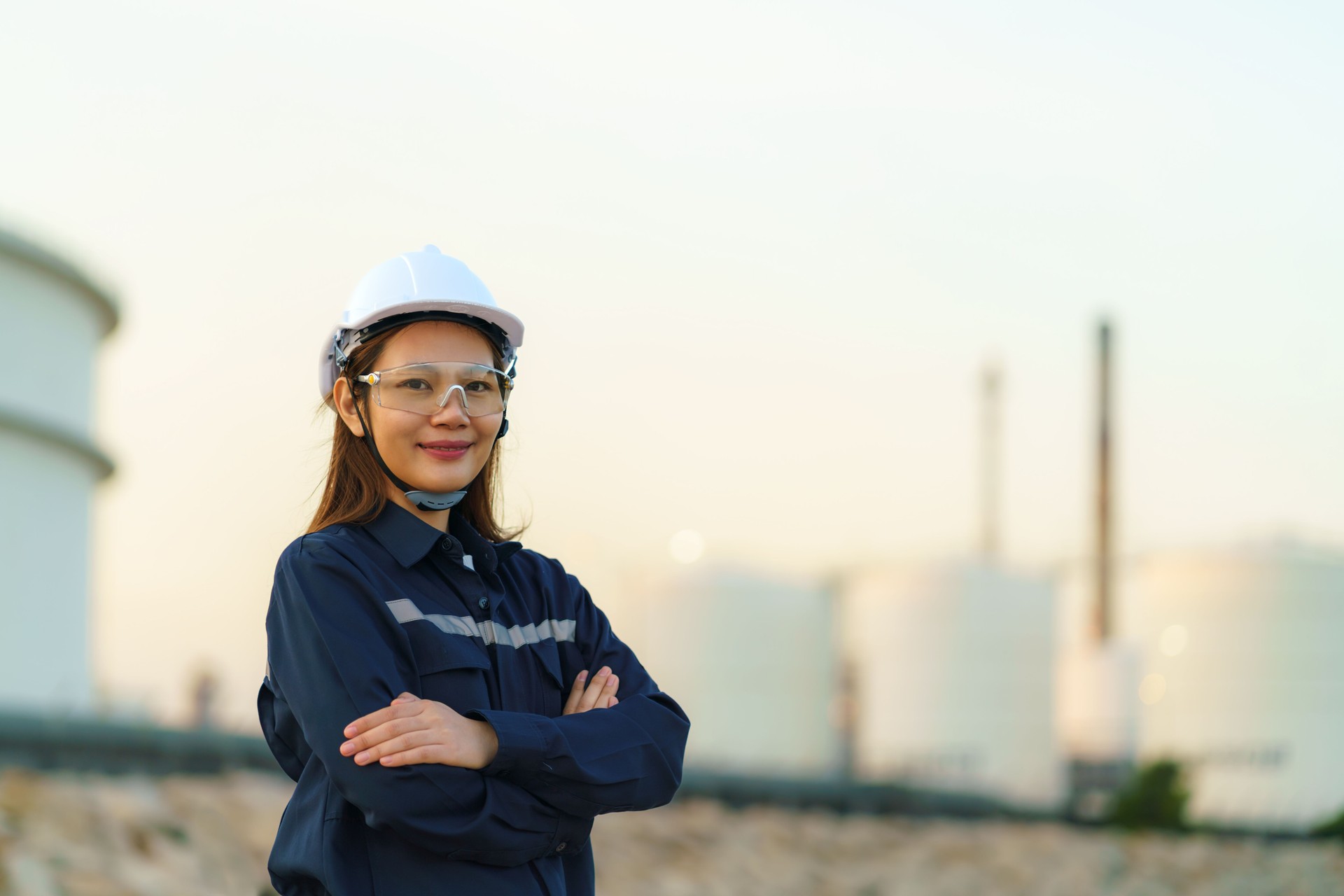 Asian woman engineer arm crossed and smile with confident looking forward to future with oil refinery plant factory in background.